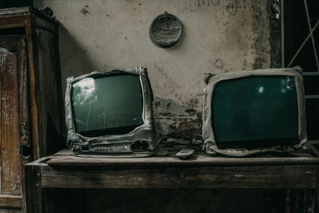 Two burnt vintage televisions in a decaying room evoke nostalgia and decay.
